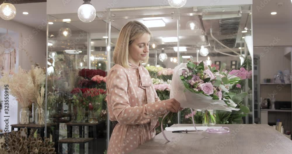 Florist woman wrapping flowers in paper at flower shop. Small business owner and beautiful florist woman Florist woman wrapping flowers in paper at flower shop. Small business owner and beautiful florist woman