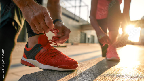 Exercising together. Close up photo of two people in sport clothes tying shoelaces before jogging outdoors. Fit, fitness, exercise