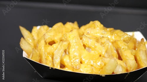 Slow motion crispy golden hot steamy french fries with melted shredded cheddar cheese