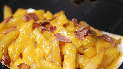 Slow motion of person sprinkling cooked crispy bacon on hot golden french fries with melted shredded ceddar cheese photo