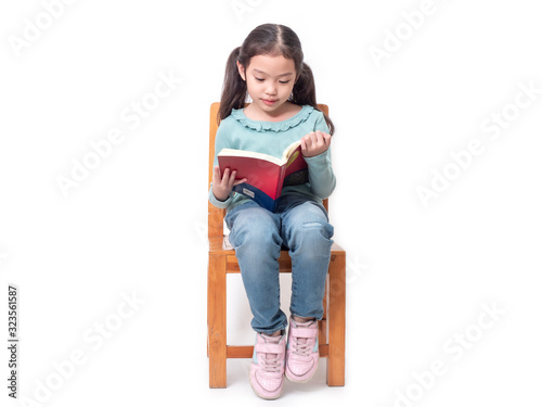Asian little cute girl 6 years old sitting on wood chair and reading the book. Preschool lovely kid with the book. Learning and education of kid.