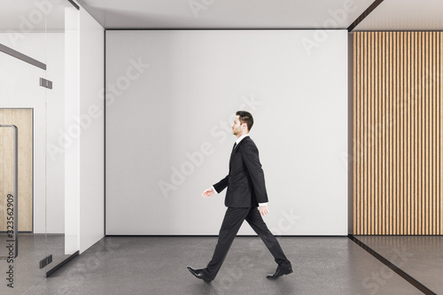 Businessman walking in office with copy space on wall.