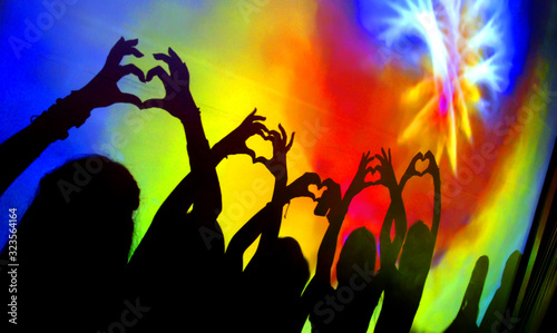 silueta de las manos de personas formando corazones en un baile con las luces de las discotecas de fondo