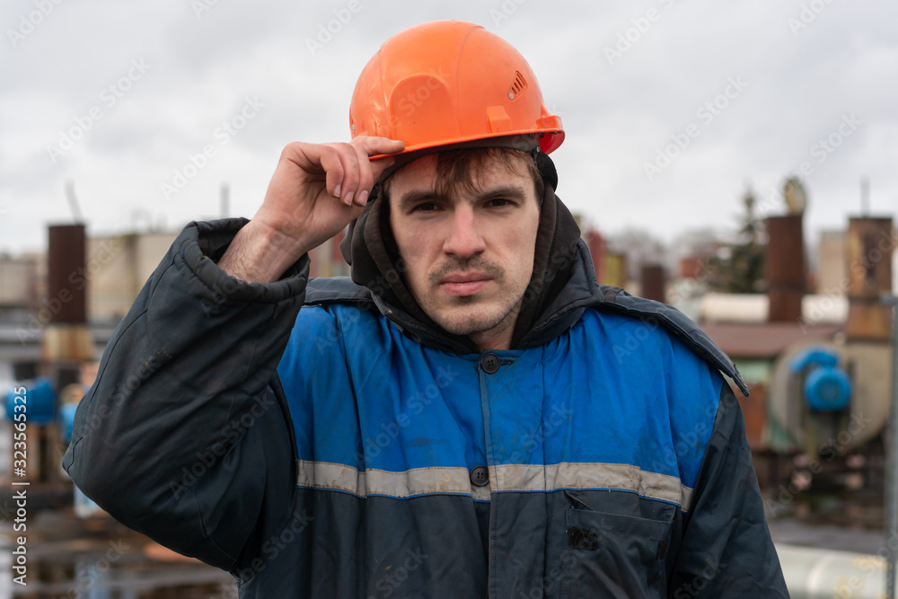 Portrait of a builder in a helmet and working dirty uniform. holds a hard hat. worker on the roof of the factory. Portrait of a builder in a helmet and working dirty uniform. holds a hard hat. worker on the roof of the factory.