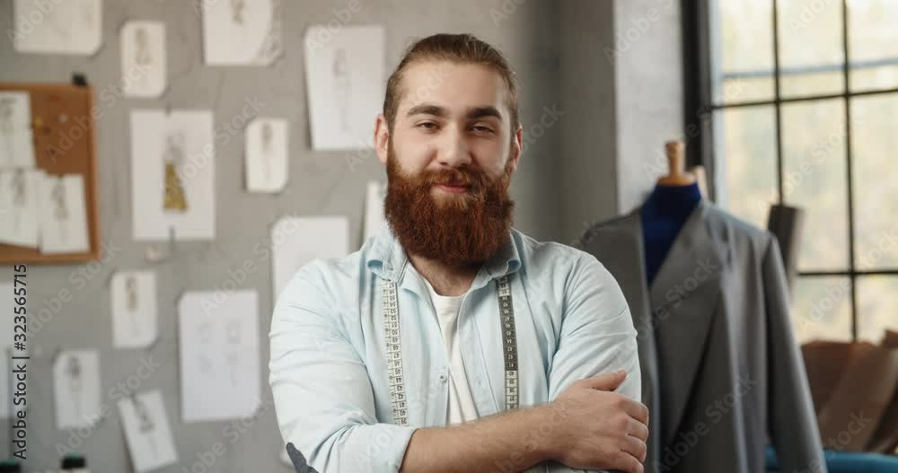 Close-up portrait shot of bearded hipster clothing designer working in his office, looking at camera and positively smiling - small business, fashion concept 4k footage Close-up portrait shot of bearded hipster clothing designer working in his office, looking at camera and positively smiling - small business, fashion concept 4k footage
