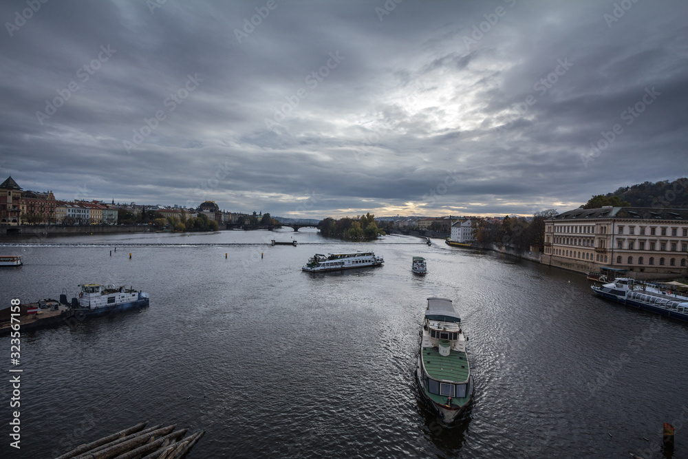 Panorama of Prague, Czech Republic, seen from the Vltava river, also called Moldau, with a focus on tourists boat and ships facing the old town, one of landmarks of the city, during sunset in autumn