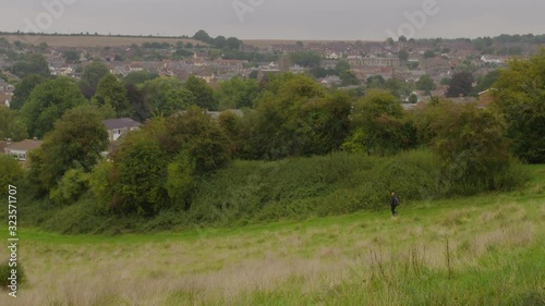 Wide shot of a hiker walking downhill on a trail, tilting up to view the city of Axminster, England photo