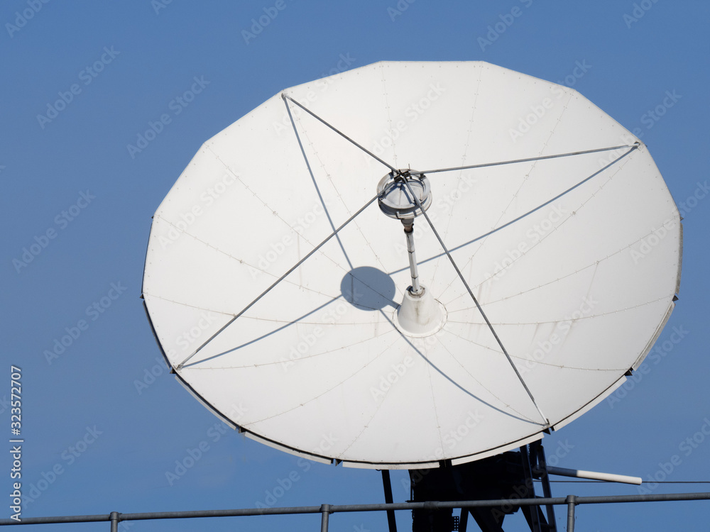 a white radio telecommunications satellite dish facing the sun