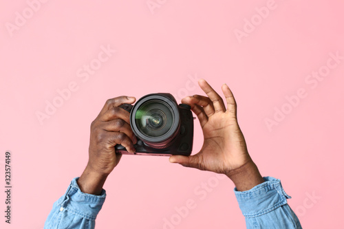 Hands of African-American photographer with camera on color background