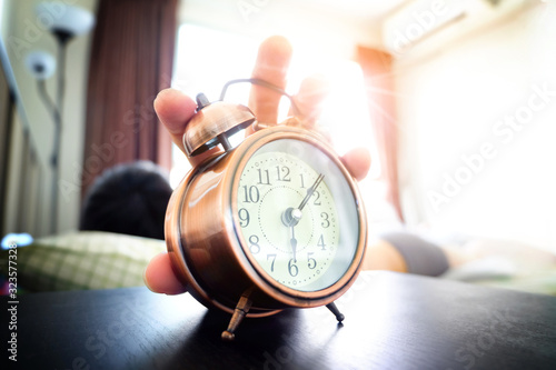 Man sleeping in a bedroom holiday. Hand holding a alarm clock in the morning. concept of health.