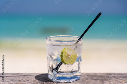Soda water with lime and ice on a wooden table near the sea on the beach
