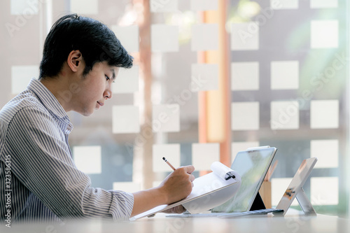 Young businessman in casual wear working with paperwork and laptop while sitting at office desk. photo