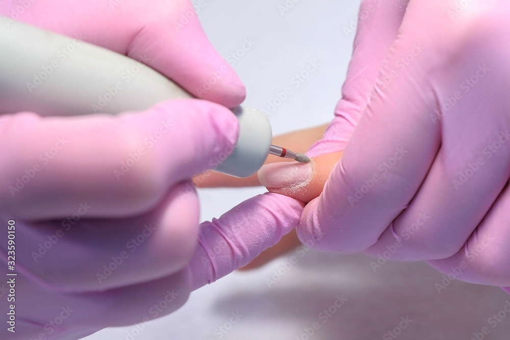 Manicure master doing manicure for client using electric nail file drill machine, hands closeup view. Hardware manicure in beauty salon for woman. Polishing skin cuticle around nail. Manicure master doing manicure for client using electric nail file drill machine, hands closeup view. Hardware manicure in beauty salon for woman. Polishing skin cuticle around nail.