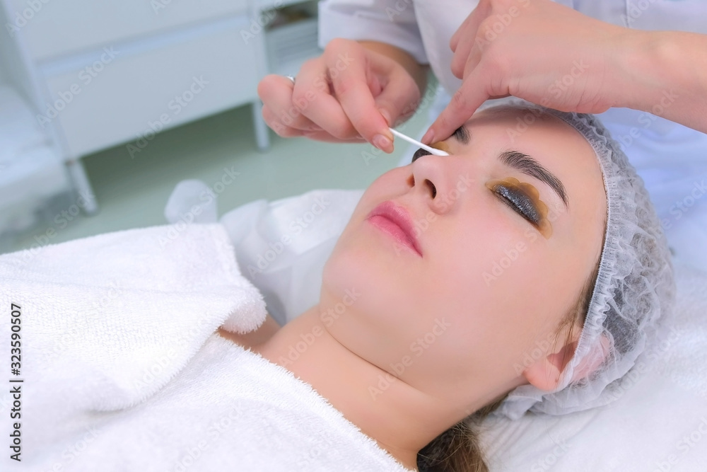 Cosmetologist wiping solution from girl's lashes using cotton stick on lift lamination procedure in clinic, woman face closeup. Beautician making lash lifting. Beauty industry concept.