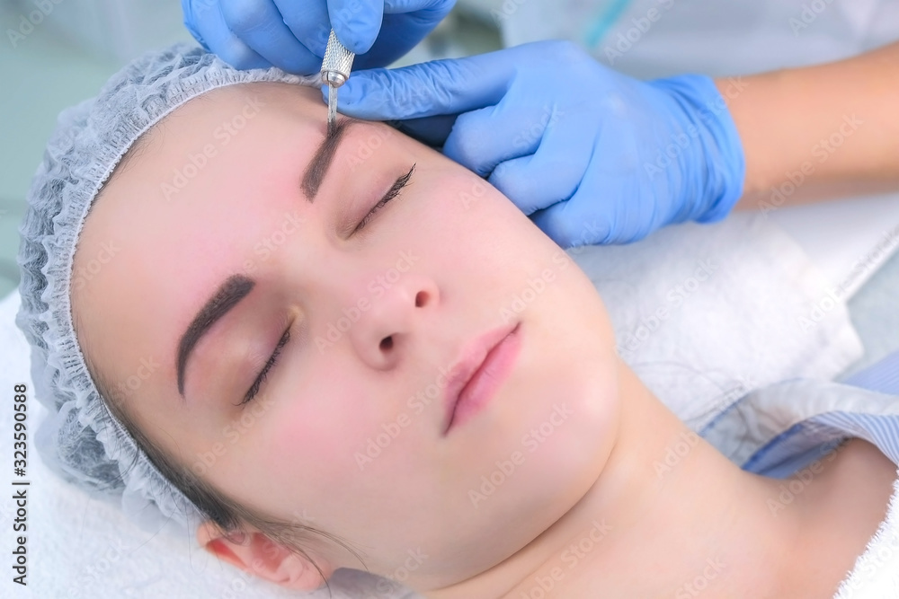 Beautician is painting shaping contour using manual tool for tattoo, woman's face closeup. Cosmetologist making eyebrows microblading procedure in beauty salon for girl. Beauty industry concept.