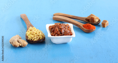 Ginger pickle, adrak ka achar, or ginger thokku, an Indian, vegetarian, and sweet and spicy side dish, with some of its main ingredients, in a white ceramic bowl.
