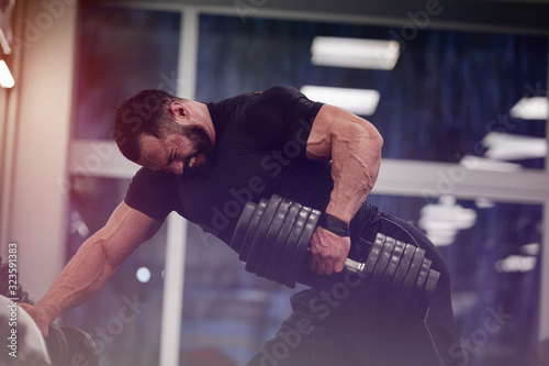Obraz na płótnie strong young man with beard wearing black sport clothes lifting heavy weight dum