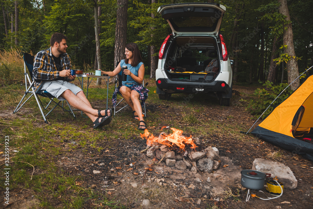 couple sitting in portable chairs drinking tea talking. camping summer activities couple sitting in portable chairs drinking tea talking. camping summer activities