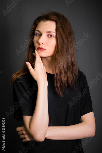 Portrait of a beautiful, young girl in black clothes with long hair. Studio photo, on a gray background. A model with clean skin.