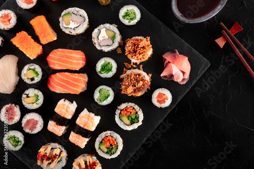 Large sushi set with soy sauce and chopsticks, top shot on a black background with copy space. A flat lay of various maki, nigiri and rolls