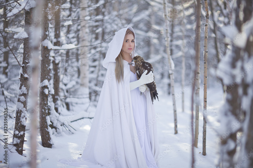 A beautiful girl in a white coat walks in the forest. The huntress with a bird in her hands.