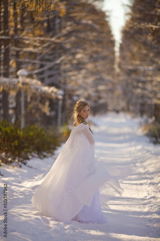 Beautiful girl in a white dress walks in the winter forest. Bride on a background of a winter landscape