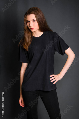 Beautiful, young girl with long hair, in black clothes, posing in studio on a gray background. A model with clean skin.