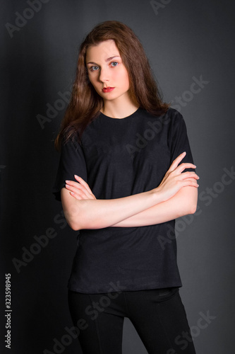 Beautiful, young girl with long hair, in black clothes, posing in studio on a gray background. A model with clean skin.
