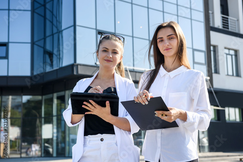 Happy women in business suits with folder standing before big business office