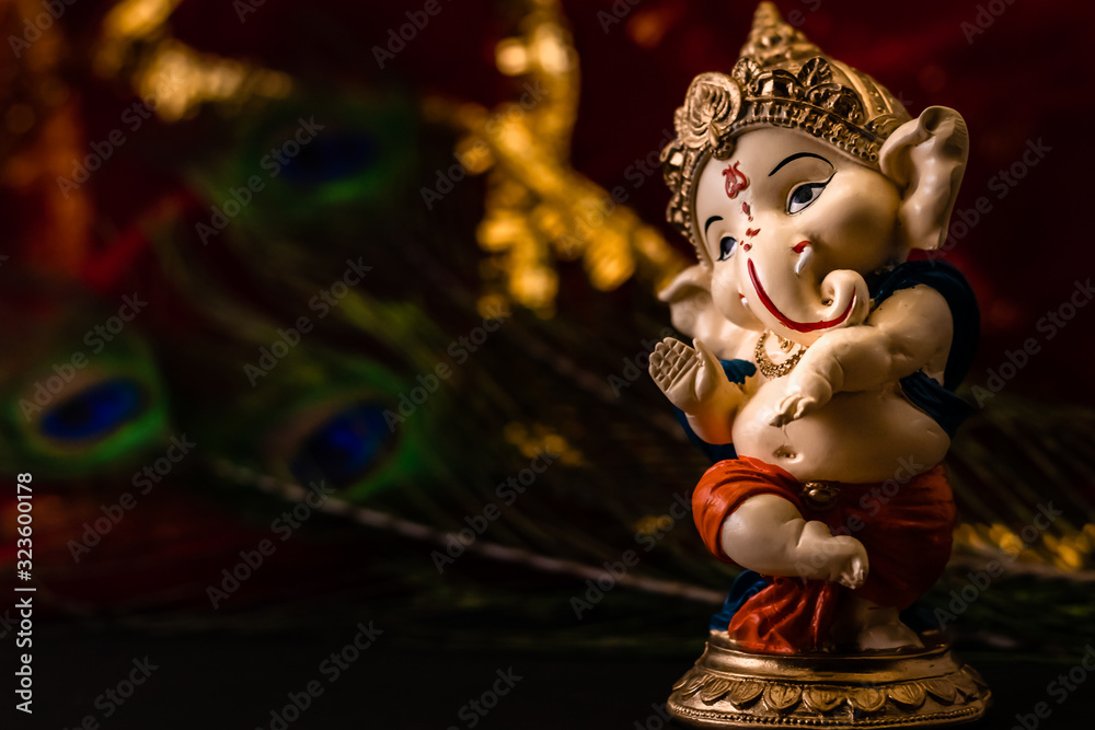 blurred red golden background with peacock feathers and ganesha statue in the foreground. religion and cultural concept.