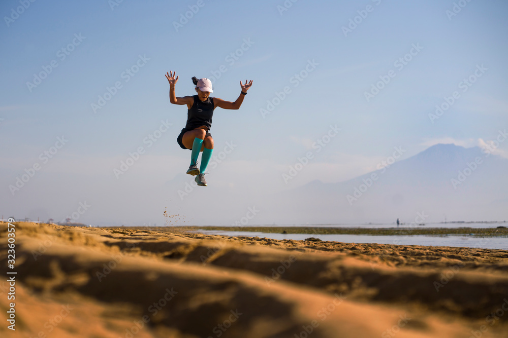 young athletic and attractive crazy happy woman jumping high on the air at beautiful beach enjoying freedom and nature during fitness workout outdoors in healthy lifestyle