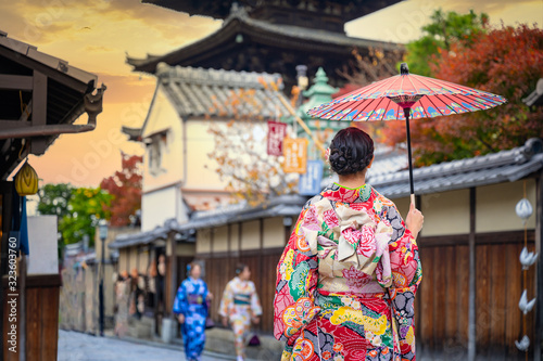 woman holding retro umbrella in old fashion style traditional kimono, walks in the middle park of garden village in autumn, travel and visit japan on incoming sport event