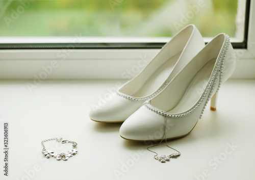 White women's shoes and jewelry are on the windowsill. Accessories for the bride