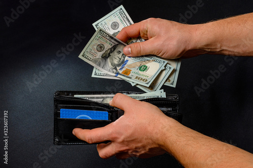 Man on black background holds in his hands a wallet with dollars close up. © Niko_Dali