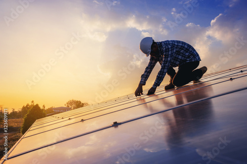 Electrical, instrument technician use wrench to maintenance electric system at solar panel field with sunset sky reflection