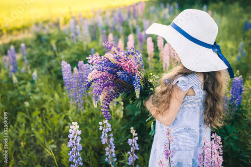 Beautiful girl in a dress and hat with a bouquet of flowers in the field