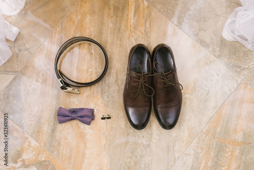 Accessories for the groom: brown shoes with laces, cufflinks, belt and purple bow tie on a beige background