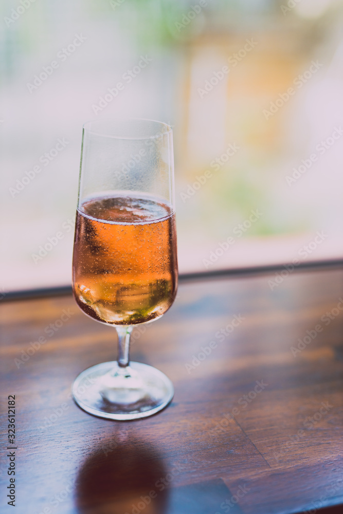 glass of chilled rose wine on wooden table next to window light with backyard bokeh glass of chilled rose wine on wooden table next to window light with backyard bokeh