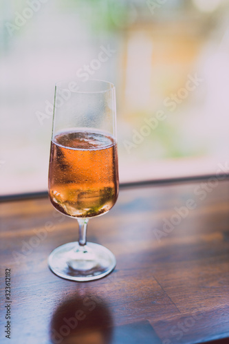 glass of chilled rose wine on wooden table next to window light with backyard bokeh