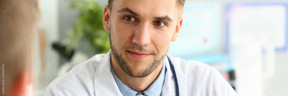 Fototapeta premium Portrait of doc wearing white uniform and striped tie. Man looking at colleague with gladness. Bearded medico having conversation with patient about work. Medical treatment concept