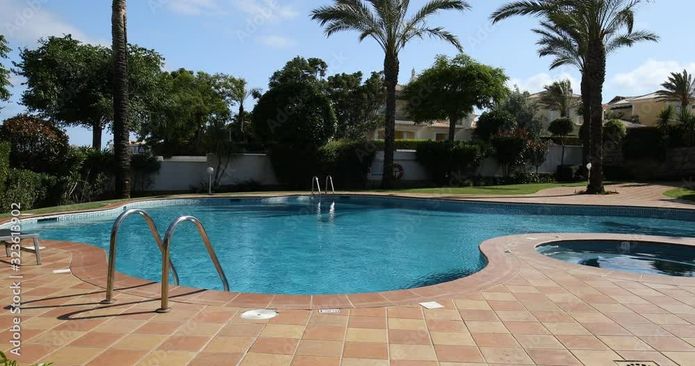 Swimming pool, sun-loungers and palm trees during a warm sunny day, paradise destination for vacations. Backyard swimming pool with garden full of palm trees and flowers. Backyard with swimming pool.