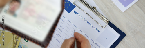 Focus on male holding identity documents and filling application for schengen visa Businessman sitting at wooden table. Travelling abroad or immigration concept. Blurred background photo