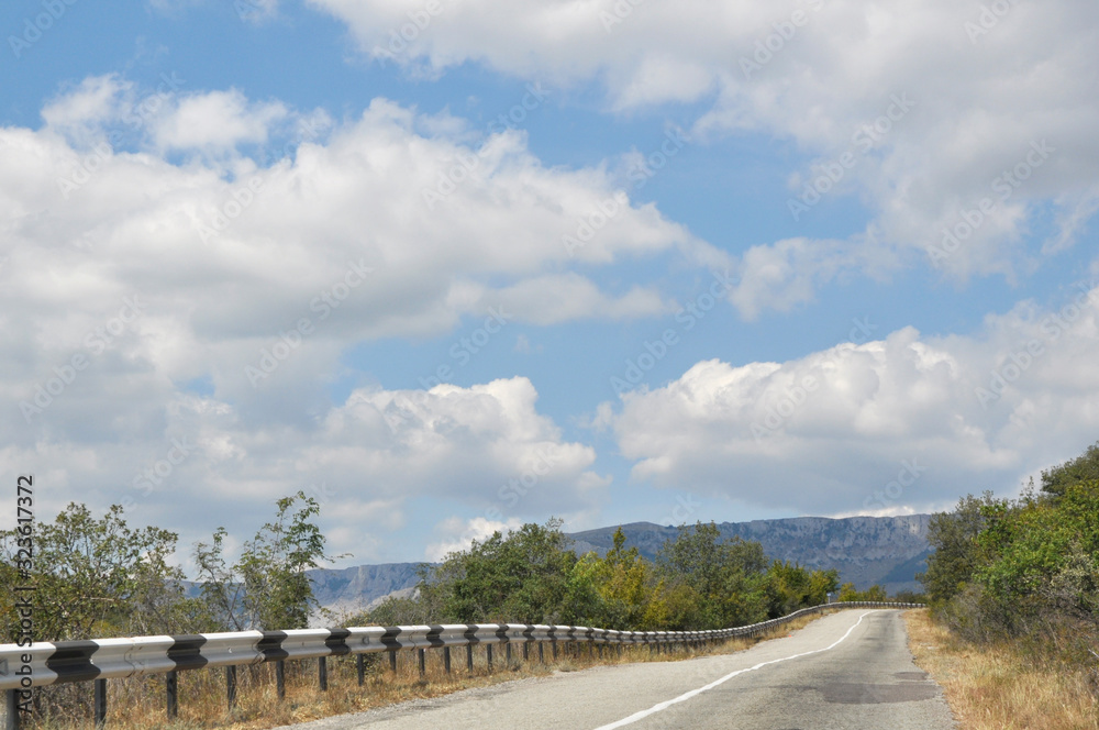 The road goes into the distance among beautiful mountains. Beautiful white clouds on the horizon The road goes into the distance among beautiful mountains. Beautiful white clouds on the horizon