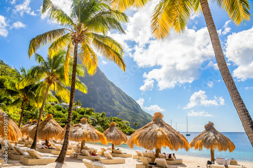 Caribbean beach with palms and straw umrellas on the shore with Gros Piton mountain in the background, Sugar beach, Saint  Lucia photo