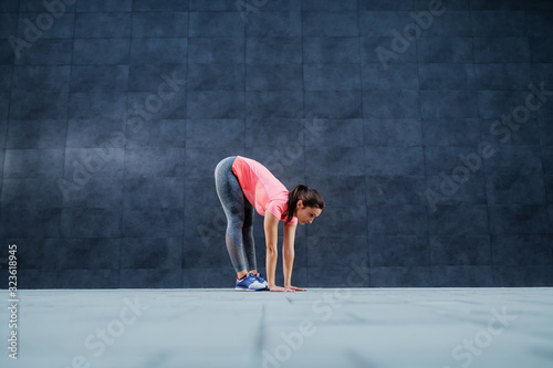 Fit caucasian sportswoman in active wear bending forward and touching ground. Stretching exercise.