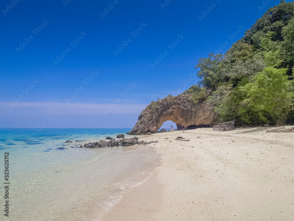 Sea view of tourists walking relax on white sand beach with green tree, rock mountain and blue sky background, Koh Khai island, Satun, southern of Thailand.
