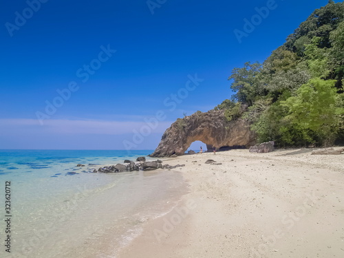 Sea view of tourists walking relax on white sand beach with green tree, rock mountain and blue sky background, Koh Khai island, Satun, southern of Thailand.