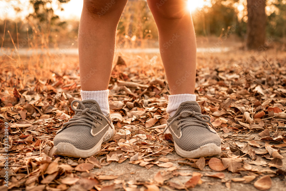 Close-up of Young girl in running shoes standing on pavement with dry leaves in summer park. Healthy lifestyle concept.