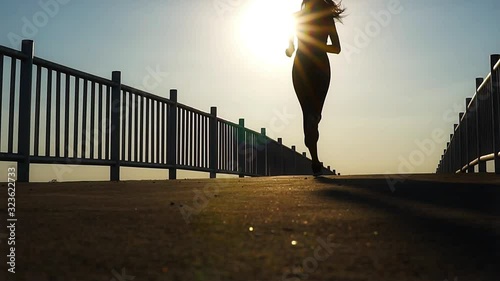 silhouette of fit woman jogging workout across the bridge while marathon practicing at the sunset