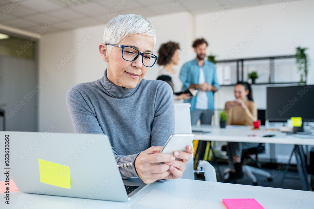 A businesswoman sitting at her office desk and using her phone. A businesswoman sitting at her office desk and using her phone.